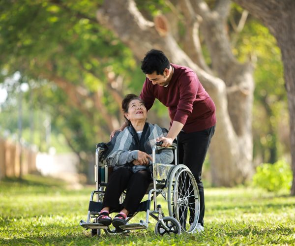 asian-senior-woman-sitting-wheelchair-with-her-son-happy-smile-face-green-park-min